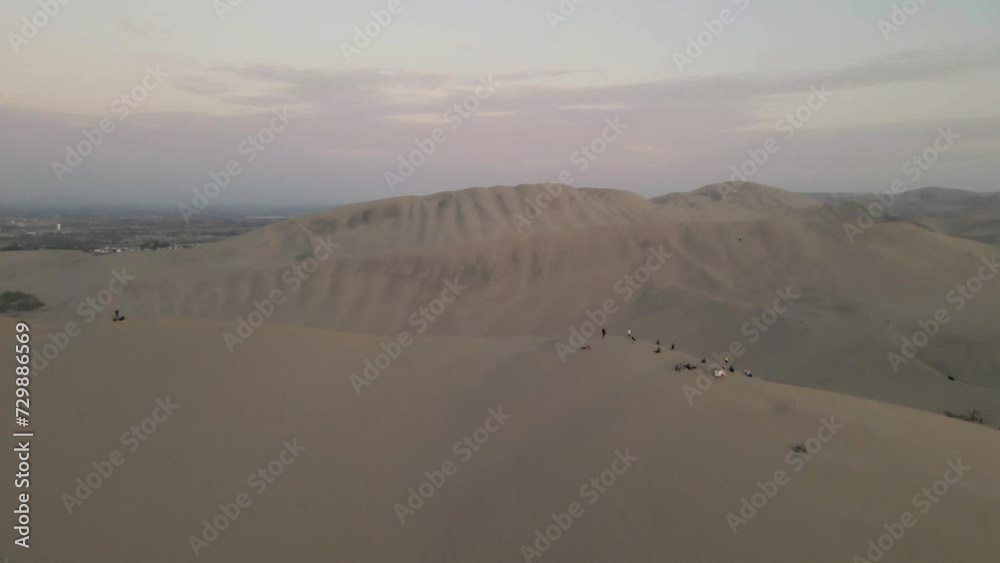 Drone gracefully soars over the dunes, passing by people, revealing the oasis gem, Huacachina. Drone gracefully soars over the dunes, passing by people, revealing the oasis gem, Huacachina.