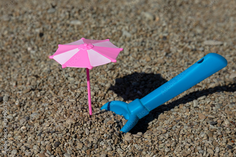 Toy pink umbrella and blue spade on the beach. Travel and holidays with children. Toy pink umbrella and blue spade on the beach. Travel and holidays with children.