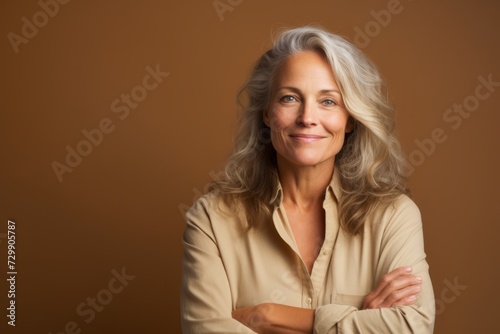 Portrait of happy senior woman with arms crossed against brown background. © Inigo
