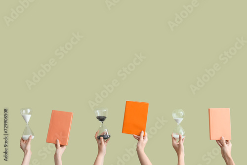 Female hands holding hourglasses and books on green background