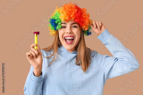 Beautiful young happy woman in funny disguise with party whistle on brown background. April Fools Day celebration
