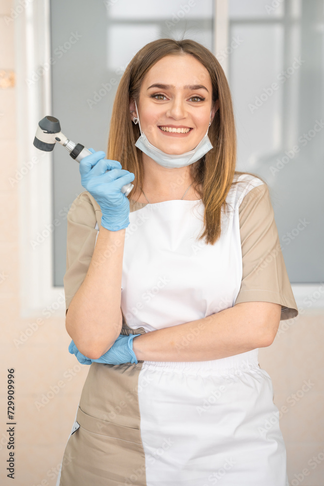 Woman dermatologist with dermatoscope in uniform and gloves in doctor office, examination room in clinic