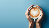 hand holding a cup of coffee with foam forming love on a blue background with copy space