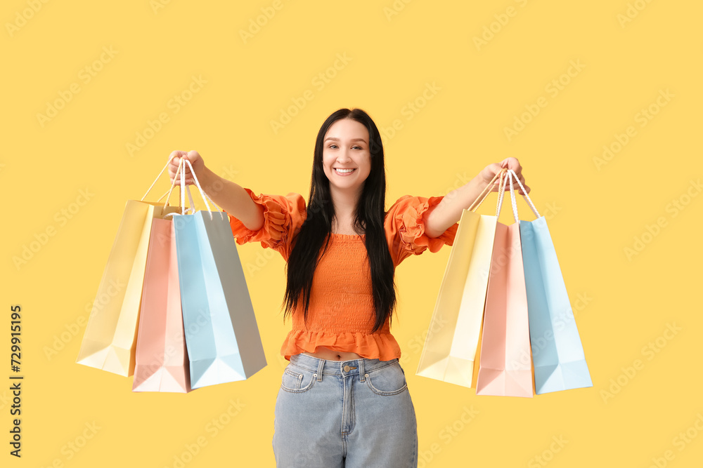 Happy young woman with shopping bags on yellow background. International Women's Day