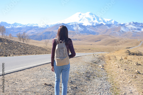 Obraz na płótnie A female traveler with a backpack on her back admires the snow-covered Elbrus on a clear autumn day. View of Elbrus, North Caucasus, Russia w salonie