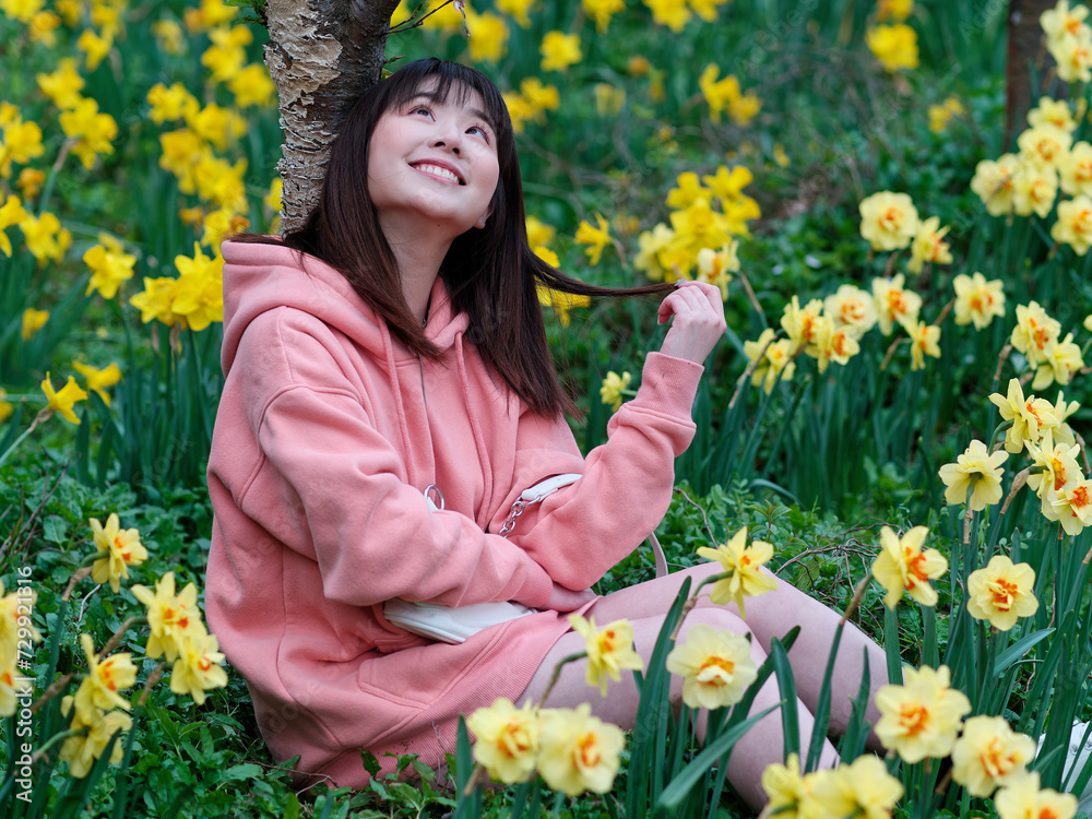 Beautiful young Chinese woman sitting in yellow daffodil flower field smiling and looking upwards. Candid happy moment. Emotions, people, beauty, youth and lifestyle portrait. Beautiful young Chinese woman sitting in yellow daffodil flower field smiling and looking upwards. Candid happy moment. Emotions, people, beauty, youth and lifestyle portrait.