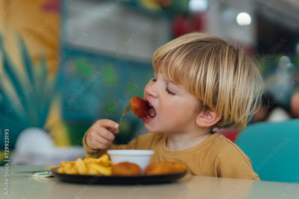 happy boy with blond hair eats fries and nuggets in restaurant happy boy with blond hair eats fries and nuggets in restaurant