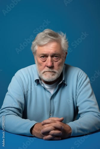 An elderly man is seen sitting at a table, his hands folded, in a calm and composed manner.