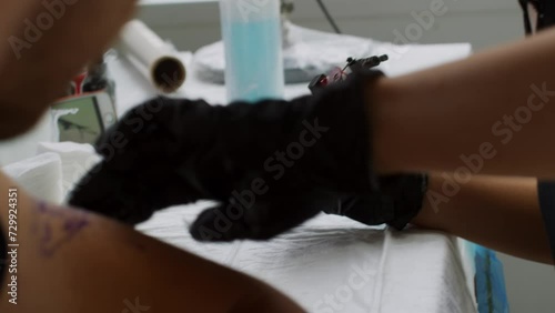 Close up shot of tattooist artist holding tattoo gun and wiping skin on arm of male client before making tattoo in studio photo