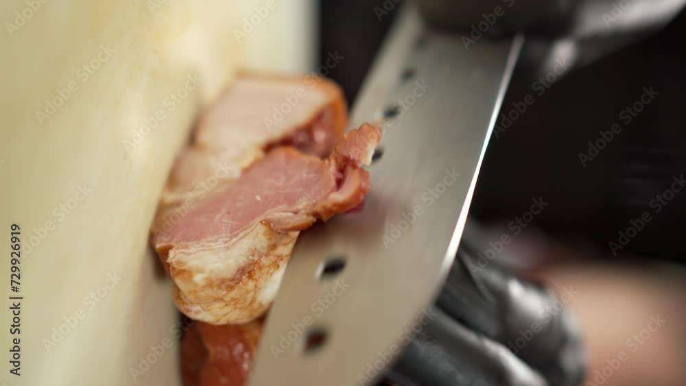 Close-up of a chef cut smoked bacon into thin slices on cutting board with a sharp Chinese knife. Bacon is one of the favorite additions to eggs and hamburger