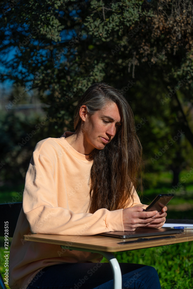 Obraz premium Middle-aged Caucasian woman working from her home garden with a desk and cell phone