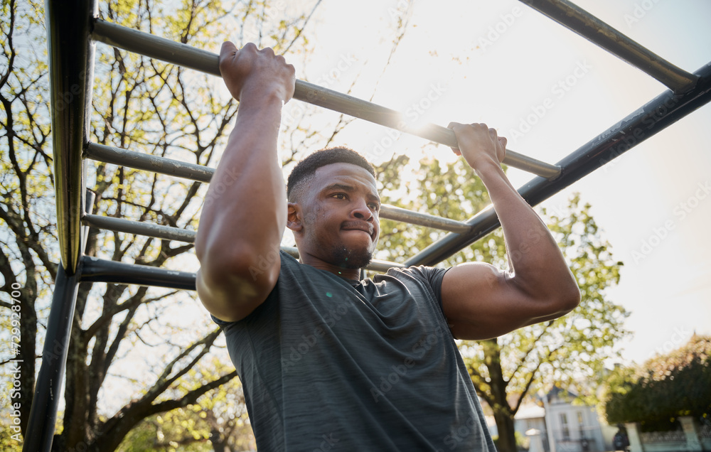 Fototapeta premium Athletic young black man in t-shirt doing pull-up on monkey bars in park