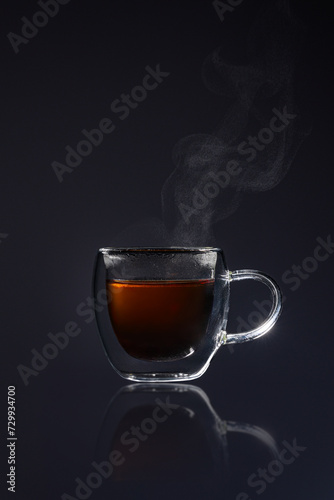 Steamy hot tea in a small glass against a black backdrop. Perfect for cozy café vibes or illustrating a calming moment