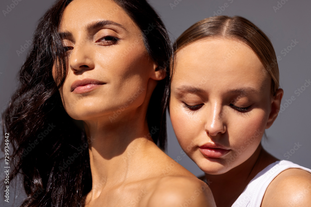 Beauty portrait of two attractive young women with clean healthy skin and hair. Charming models with natural makeup on a gray isolated background. Beauty portrait of two attractive young women with clean healthy skin and hair. Charming models with natural makeup on a gray isolated background.