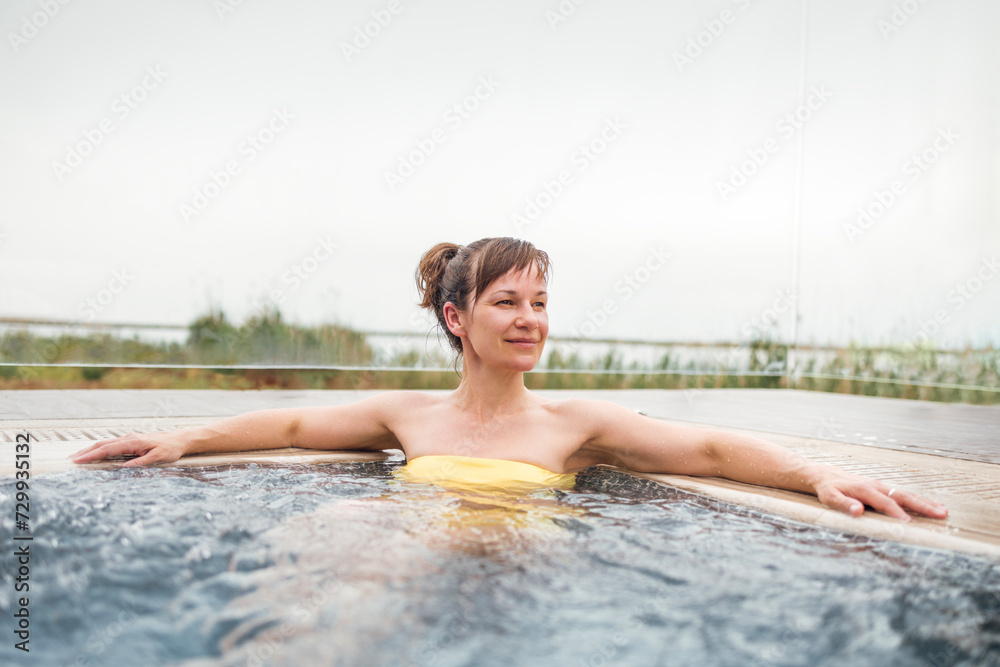 A happy young woman enjoy the time spent at the weekend in the pool. Pretty female in yellow swimsuit are sitting in the bubbling water.