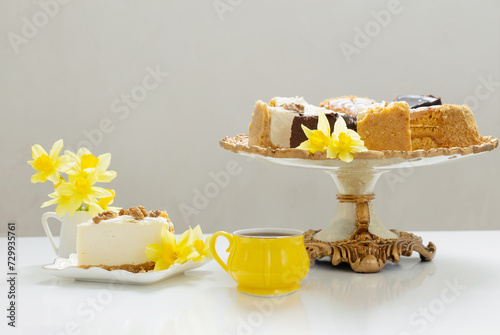 cheesecake with cup of coffee and yellow spring flowers on white table