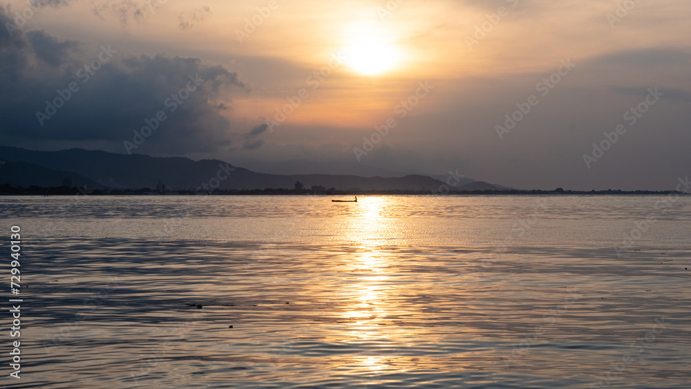 Scenic landscape of silhouetted local fishermen in a traditional wooden fishing canoe boat with golden sunset reflecting over ocean on tropical island of Timor-Leste in Southeast Asia