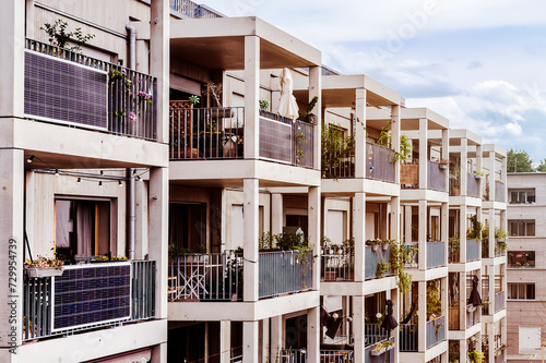 Modern Facade of Multifamily Building with Mini Solar Panel Energy System or Small Photovoltaic Plant on Balcony Railings in Apartments.