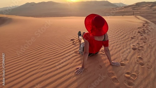 A girl its in red on the Omani sand, witnessing the sun emerge from the mountains in Empty quarter desert of Oman or Rub' al-Khali. photo