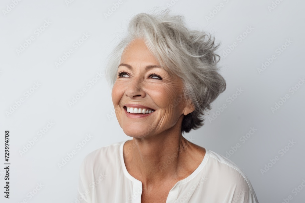 Portrait of a happy senior woman smiling at camera against grey background Portrait of a happy senior woman smiling at camera against grey background