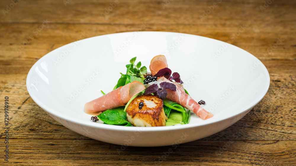 Scallop and ham appetizer with caviar on white plate on wooden table in restaurant Scallop and ham appetizer with caviar on white plate on wooden table in restaurant
