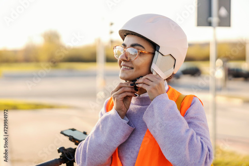 A girl is putting a helmet on while preparing for an electric scooter drive on a street.