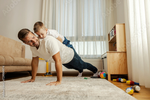 A strong father is doing pushups at home with his son on his backs. photo