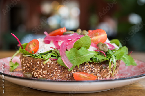 Brown bread open sandwich with salad, red onions, tomatoes and capers on a plate in a cafe restaurant