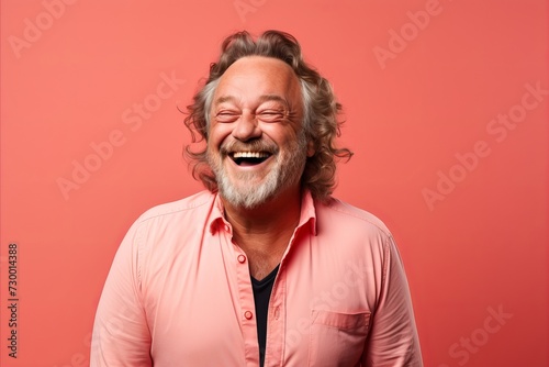 Portrait of a happy senior man laughing on a pink background.