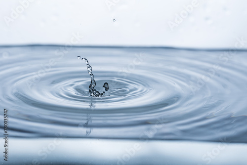 Dynamic water droplet reflecting on a clean white surface, creating a captivating splash. Ideal for advertising, product photography, or illustrating concepts of freshness and purity