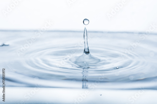A single water droplet reflects on a pristine white background. Ideal for illustrating purity, simplicity, or the beauty of natural phenomena