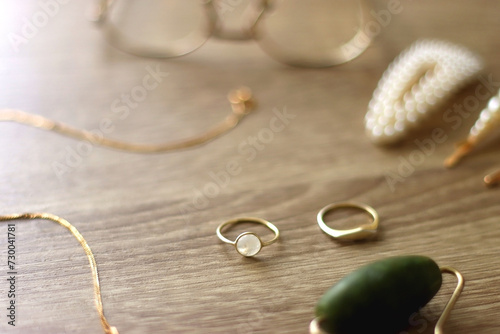 Pearl headband and barrette, golden eyeglasses, gold necklace, earrings and rings, jade face roller and hair pins on wooden background. Various elegant gold accessories. Selective focus.