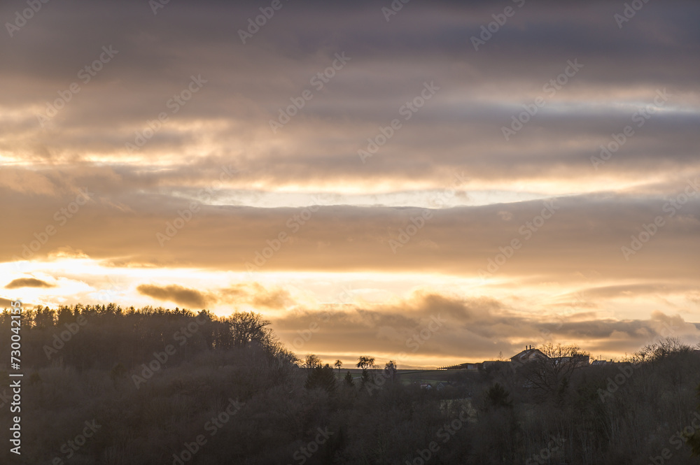 Silhouette Hochebene mit Wald, Bauernhof und Bäumen  vor Sonnenuntergang mit leuchtenden Wolken