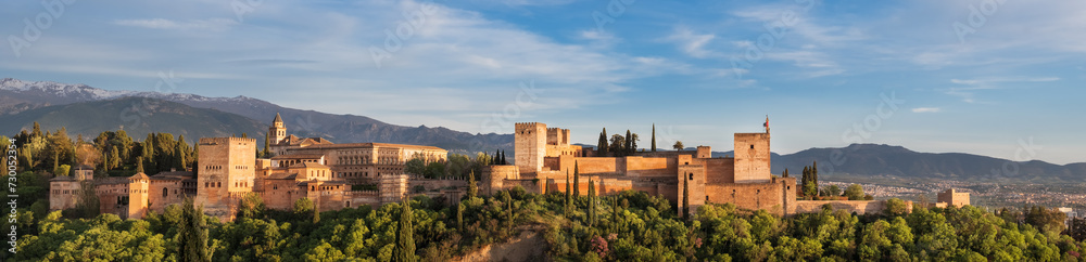 Panoramic sunset hour time of Alhambra medieval palace and fortress complex with Sierra Nevada snowy mountains in Granada, Andalusia, Spain. Known as a Capital of Nasrid Kingdom or Emirate of Granada.