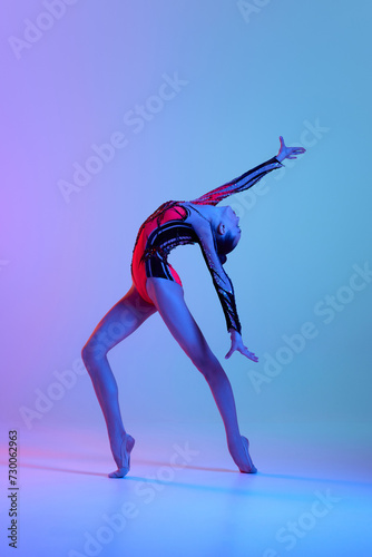 Talented, artistic teen girl in bright costume, rhythmic gymnast dancing against gradient studio background in neon light. Concept of sport, beauty and grace, competition, art, youth, hobby © master1305