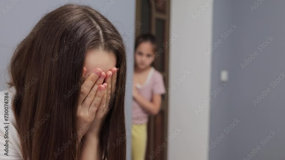 Exhausted sad depressed woman with brown haired felling stress being nervous sitting at home her little daughter worried daughter standing on background Exhausted sad depressed woman with brown haired felling stress being nervous sitting at home her little daughter worried daughter standing on background