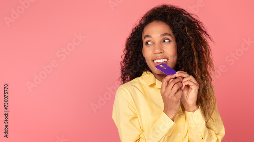 Young black woman with credit card on coral background