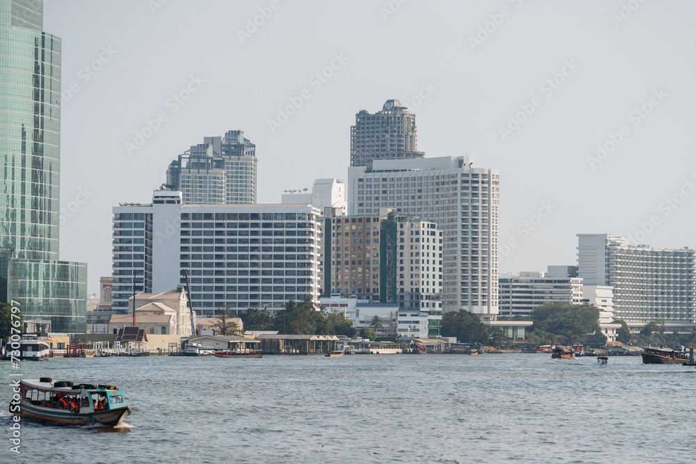 A boat cruising on the Chao Phraya River with the Bangkok cityscape in the background.