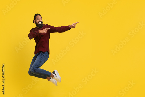 Emotional excited millennial indian guy jumping, showing advertisement