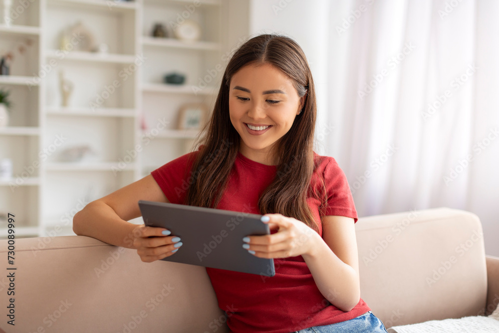Asian woman relaxing with digital tablet while sitting comfortably on modern couch Asian woman relaxing with digital tablet while sitting comfortably on modern couch