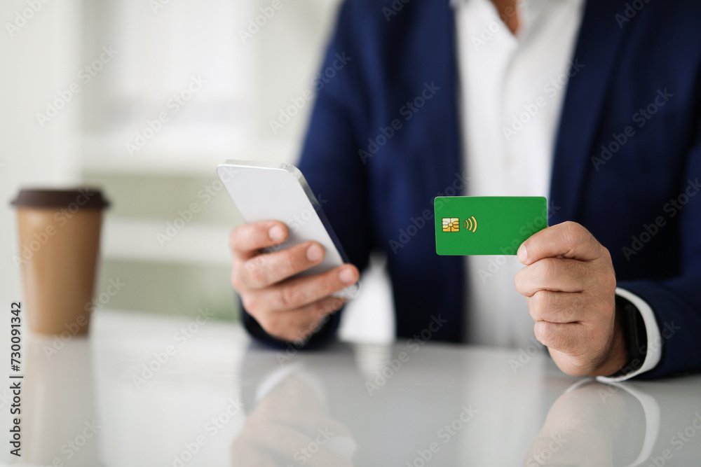 Close-up of a businessman's hands using a smartphone and holding a green credit card Close-up of a businessman's hands using a smartphone and holding a green credit card