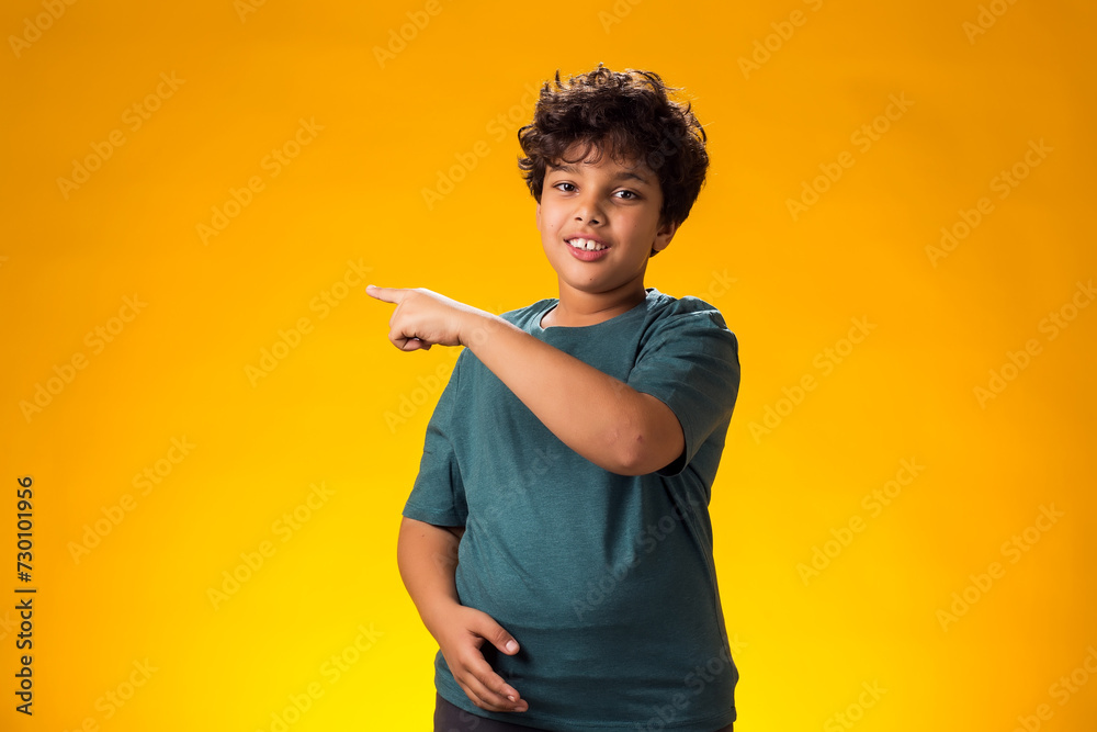 Smiling child boy pointing to an empty place on yellow background. Advertisement concept Smiling child boy pointing to an empty place on yellow background. Advertisement concept