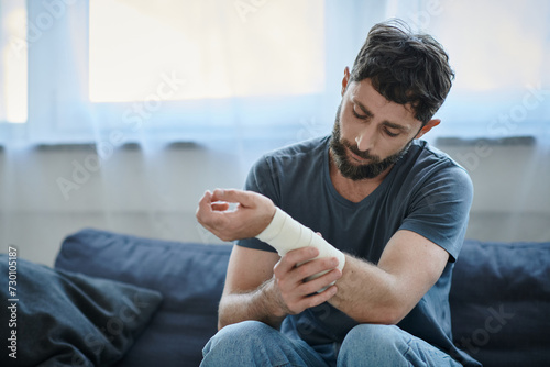 depressed man with bandage on arm after attempting suicide sitting on sofa, mental health awareness photo