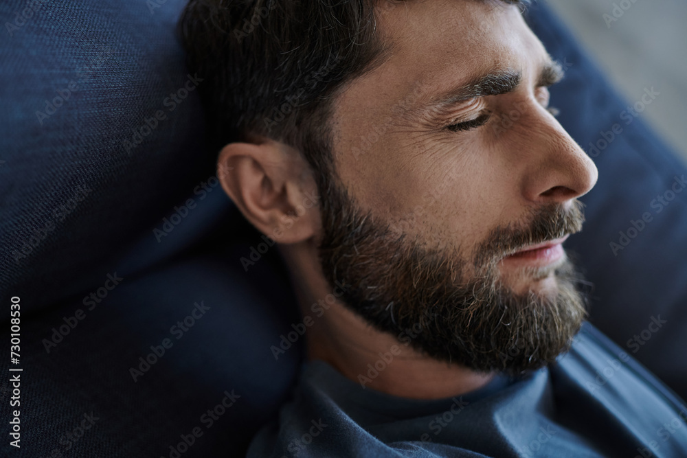 Fototapeta premium depressed anxious man with beard in casual attire lying on sofa during mental breakdown, awareness