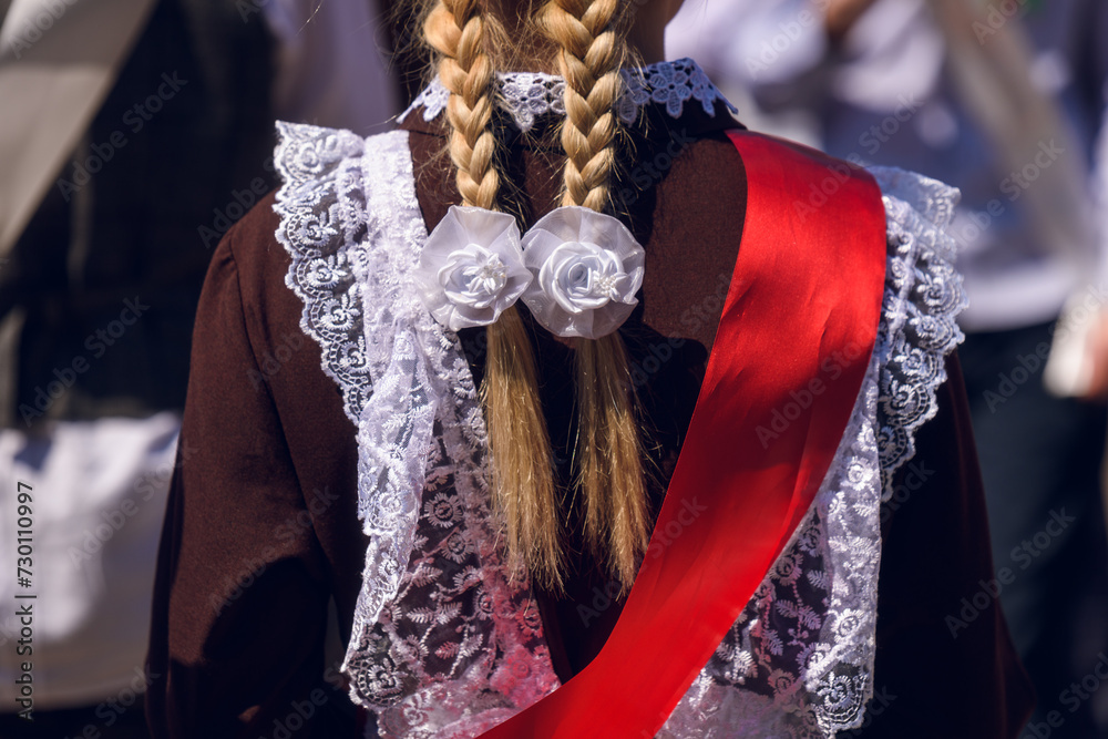 The back of a girl in a school uniform with a red graduate ribbon.