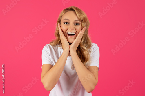 Portrait Of Excited Young Blonde Woman Cupping Face, Pink Background