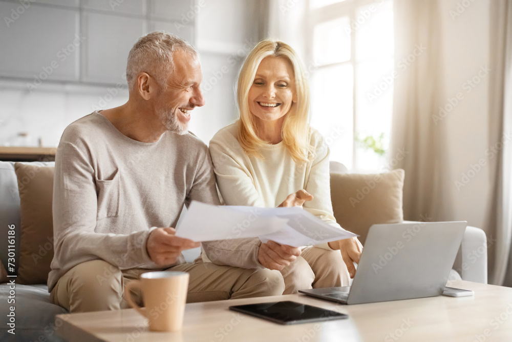 Smiling retired couple holding papers, calculating domestic bills Smiling retired couple holding papers, calculating domestic bills
