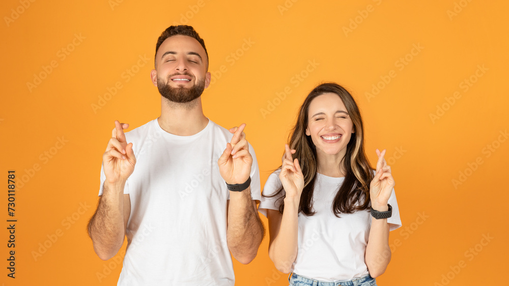Joyful young couple with eyes closed, fingers crossed for good luck