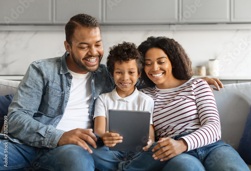 Black family with preteen son smiling joyfully while using digital tablet together