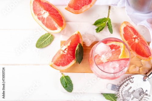 Grapefruit margarita or lemonade cocktail with cold champagne. Refreshing summer cocktail with garnish of a piece of grapefruit and mint on a light background with bar tools and ingredients